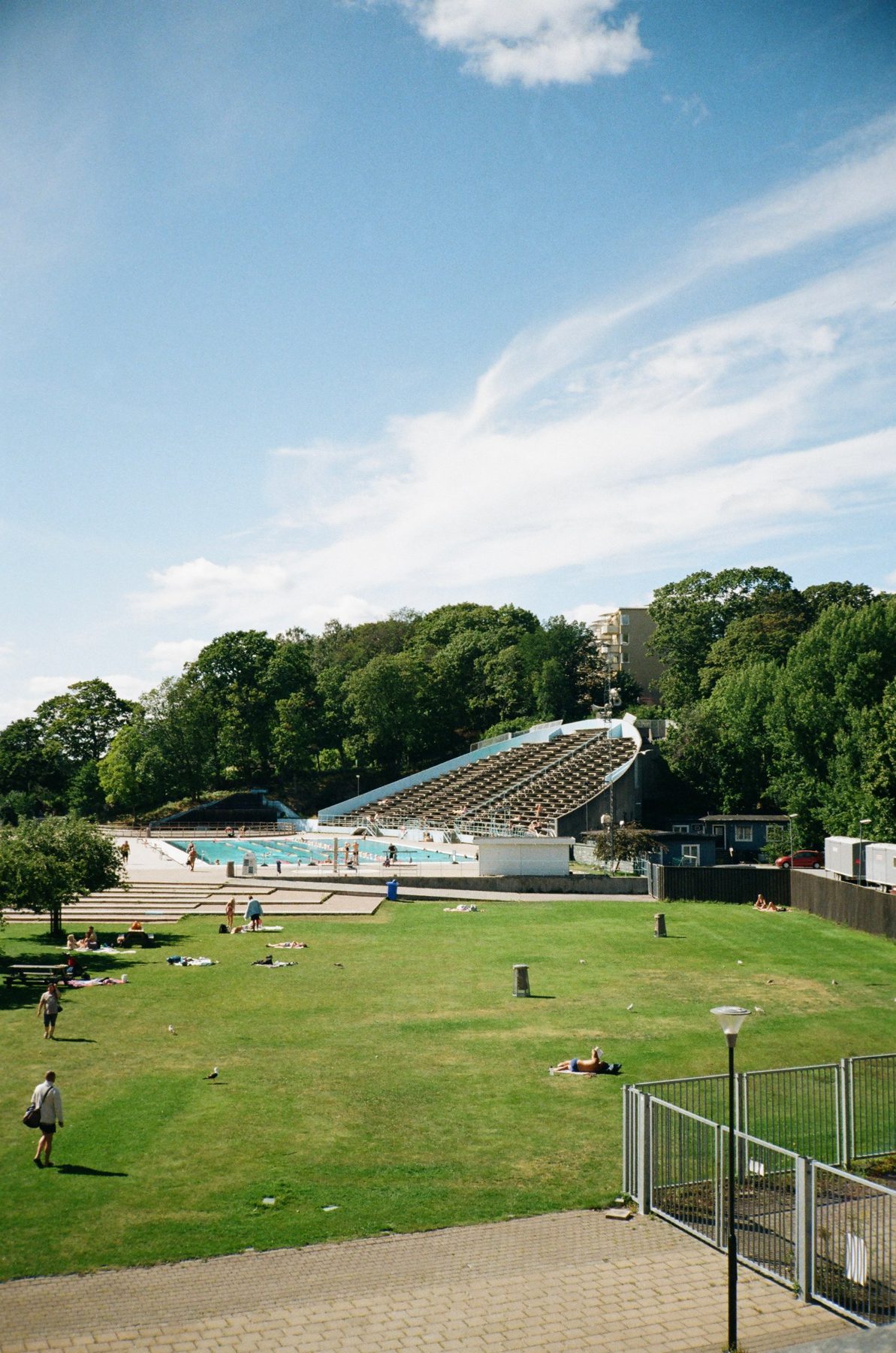 An open-air pool and sweeping concrete grandstand below a wooded hill