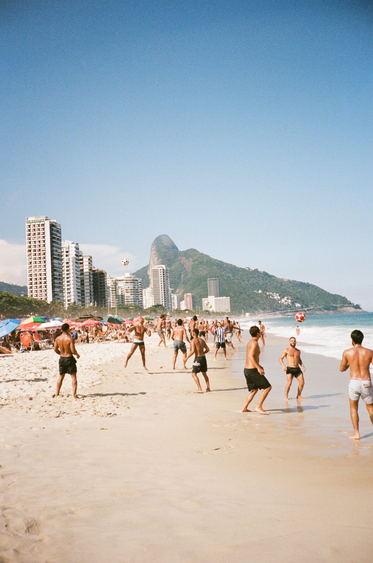 Men keeping footballs in the air along the waterline, towers and a peak behind