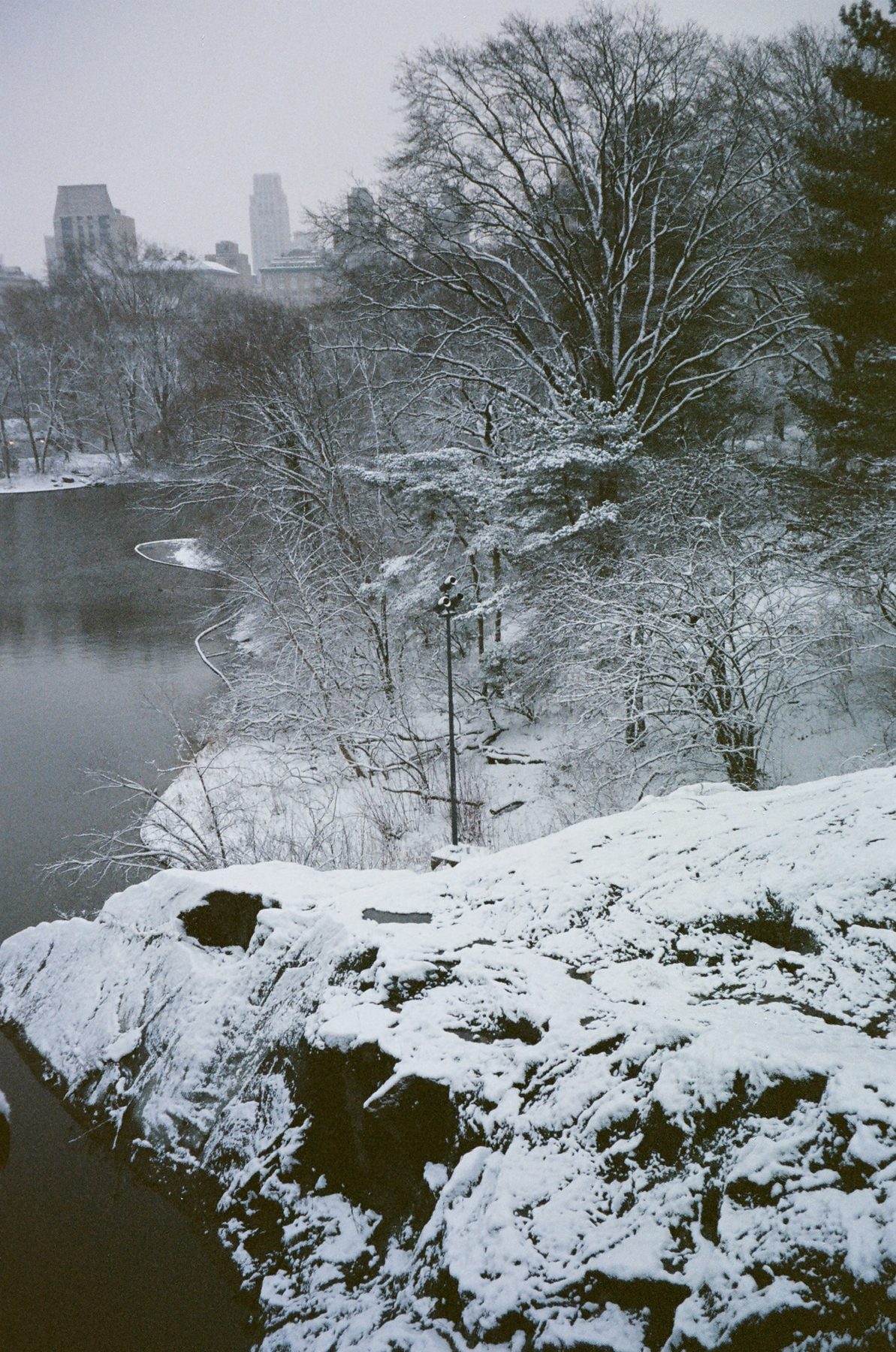 A snowy rock outcrop above the dark lake, the skyline in haze