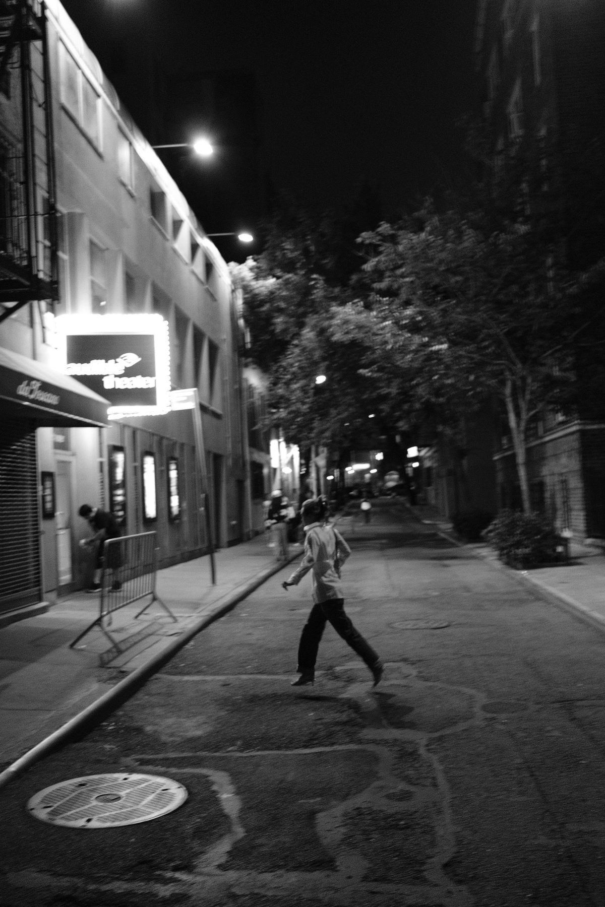 A woman skipping across the empty street past the glowing theater marquee