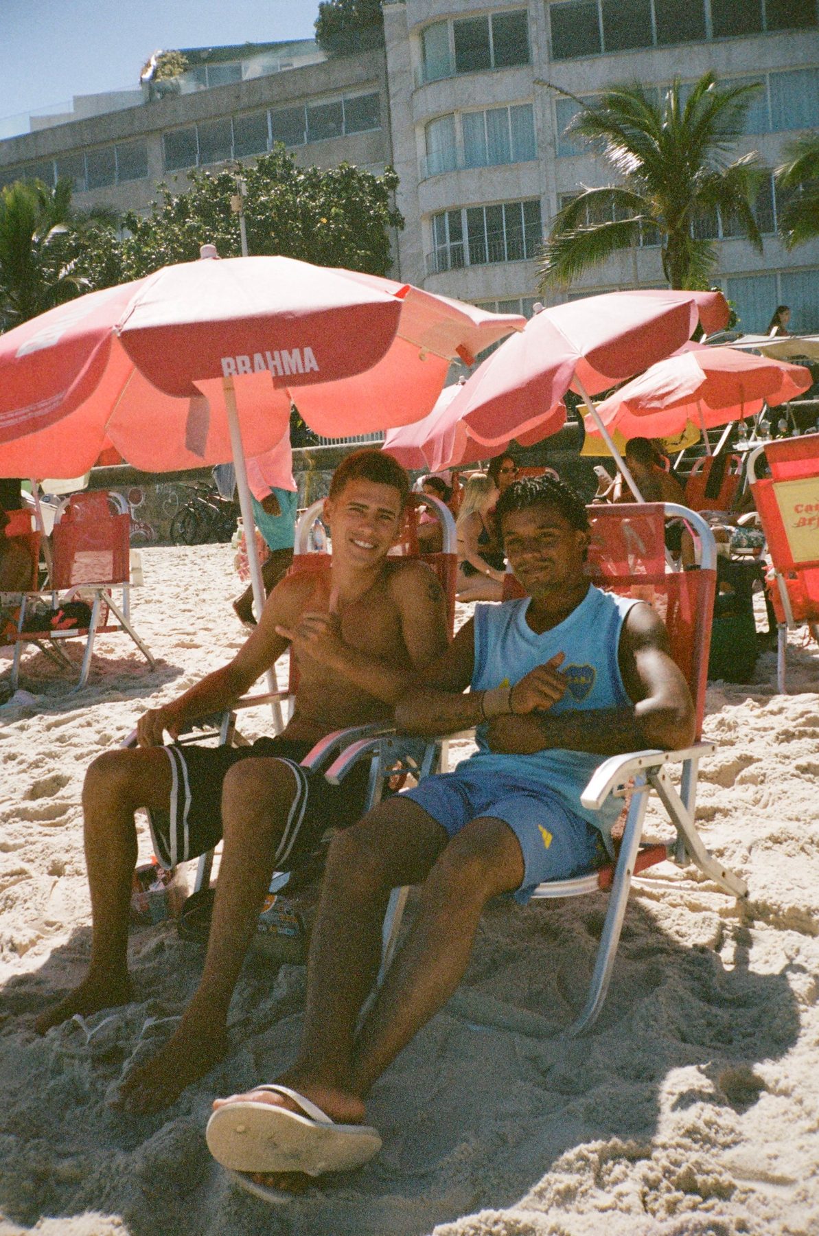 Two young men smiling in red beach chairs under Brahma umbrellas