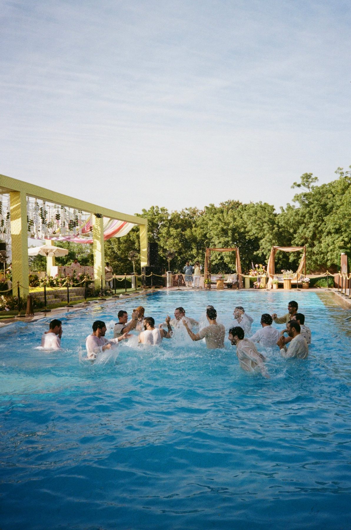 Men in soaked white shirts splashing and dancing in a bright blue pool