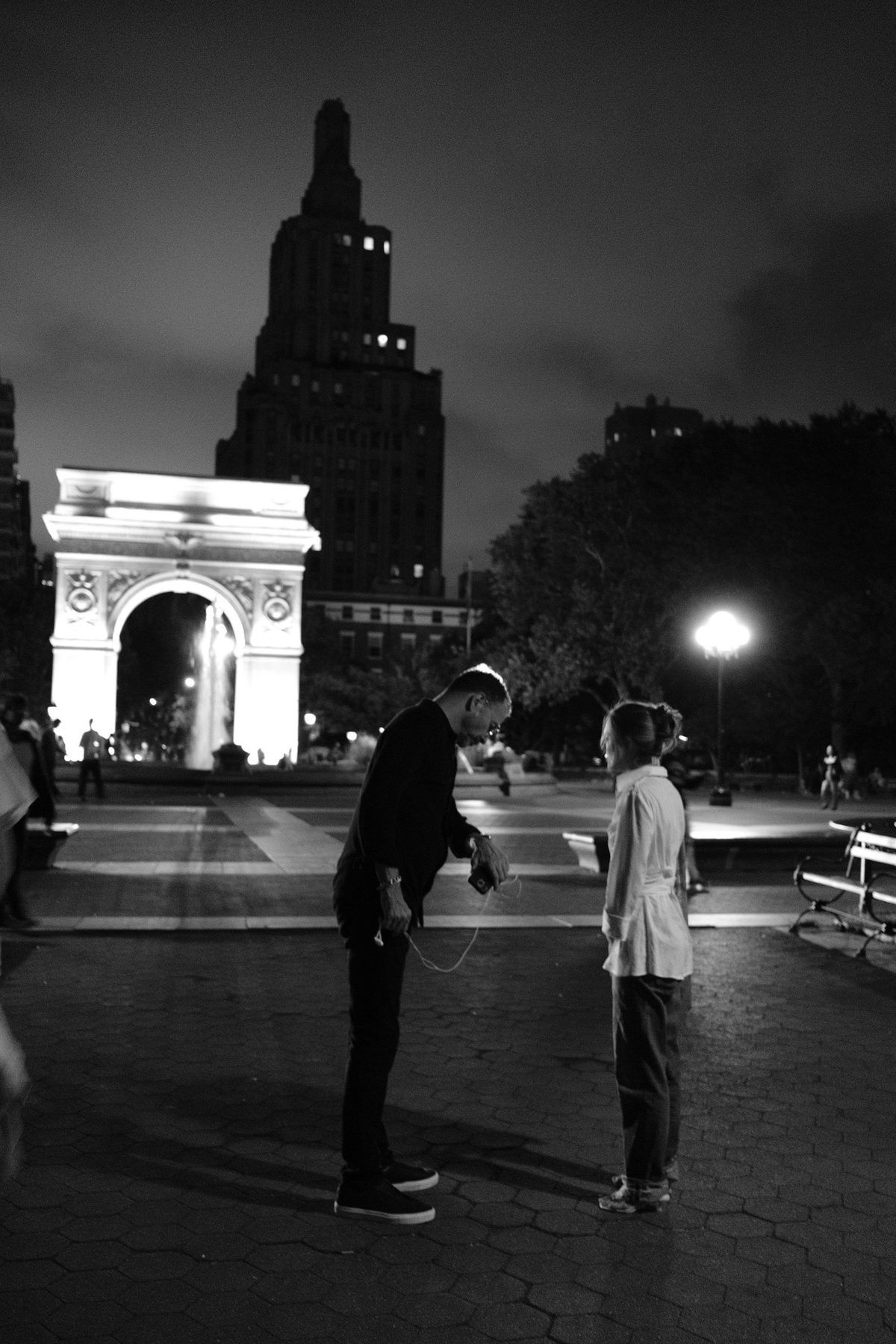 Two figures sharing earbuds before the lit Washington Square Arch