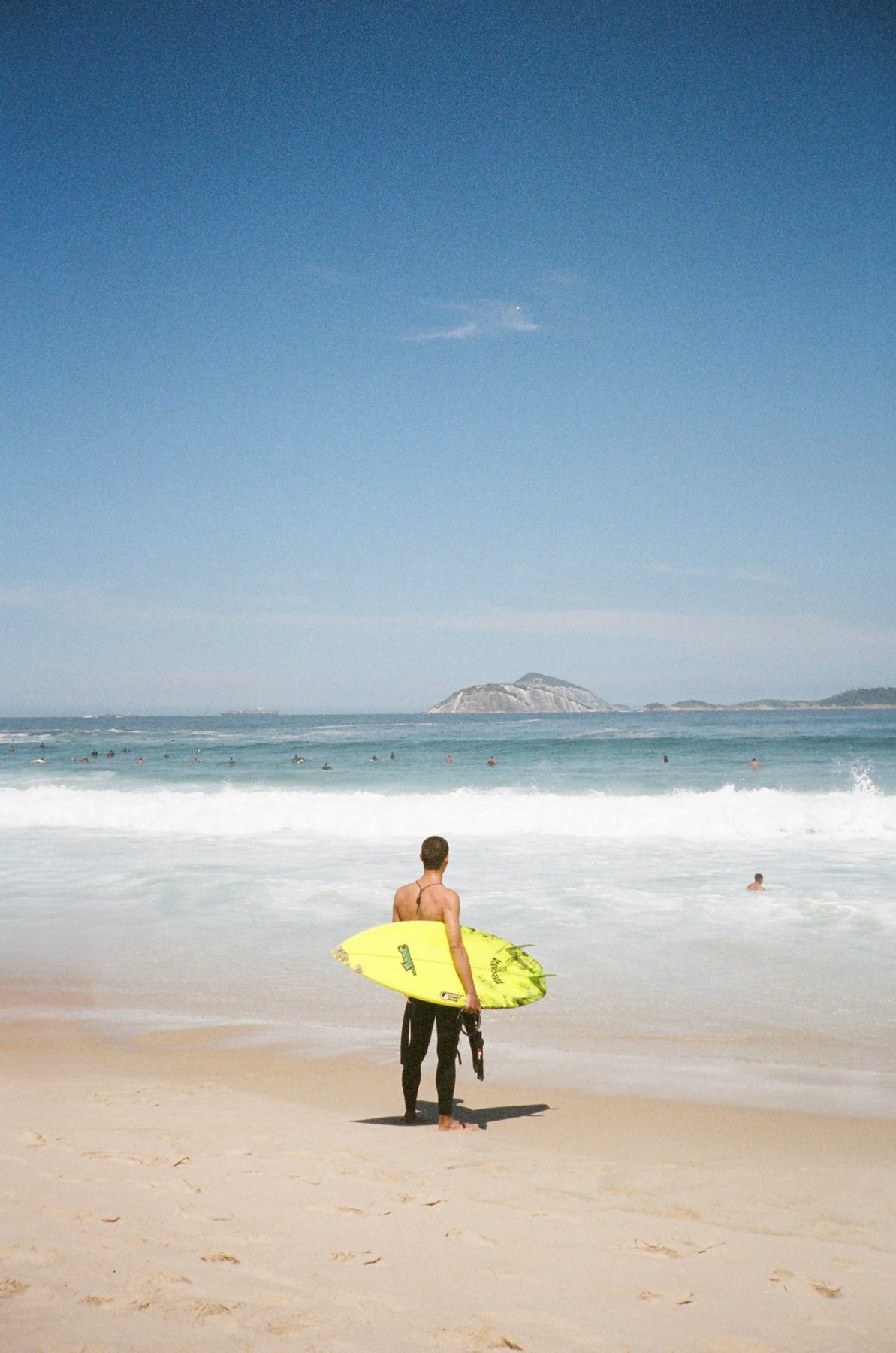 A surfer with a yellow board facing the waves and an island offshore