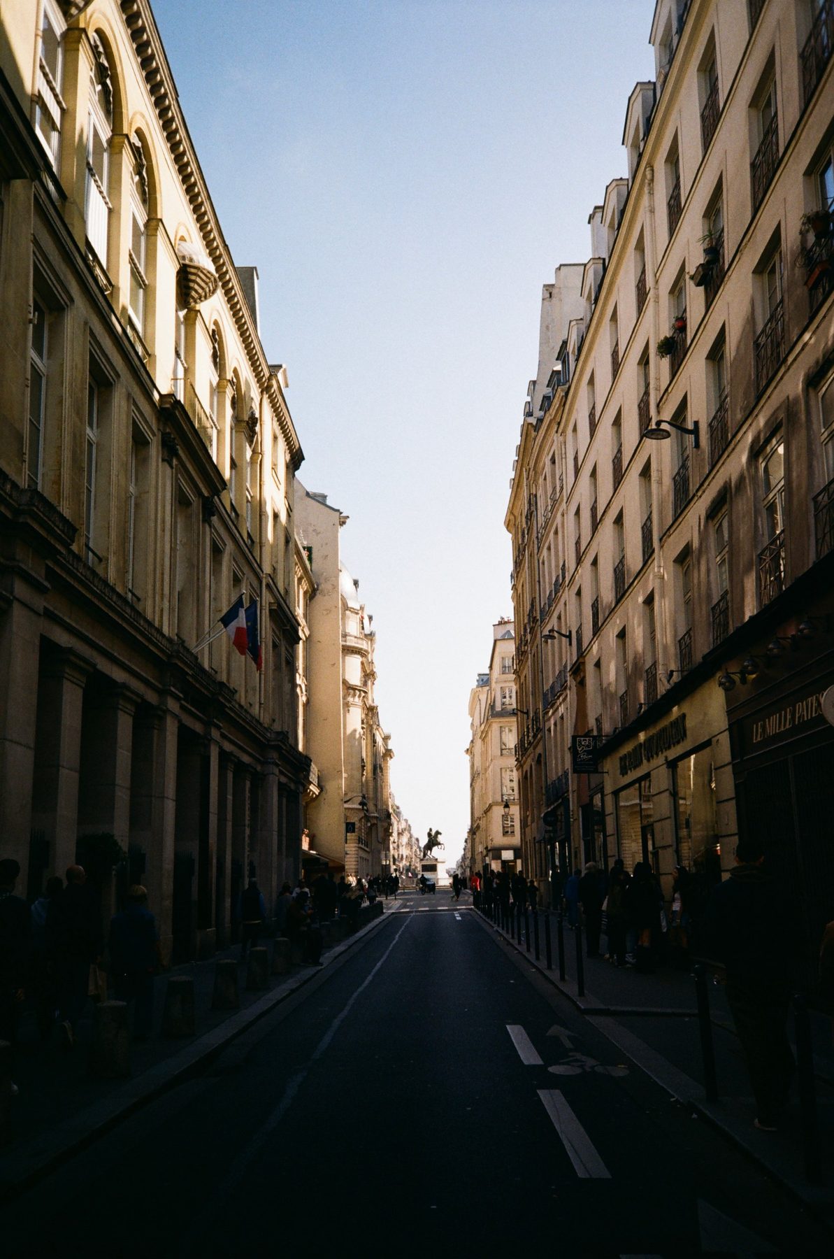 A narrow Paris street of cream facades leading to an equestrian statue