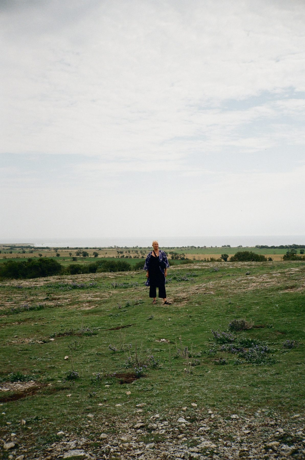 A woman in a blue kimono standing alone on a wide grassy heath above the sea