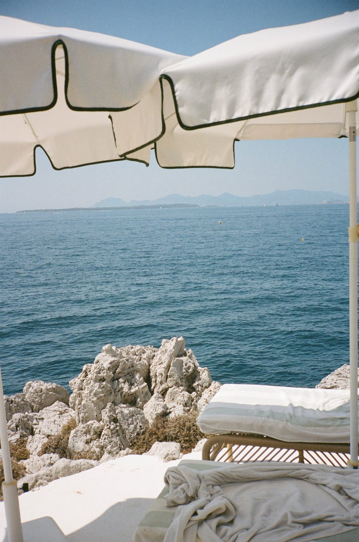 White umbrellas with black trim framing the blue sea, a lounger and robe below