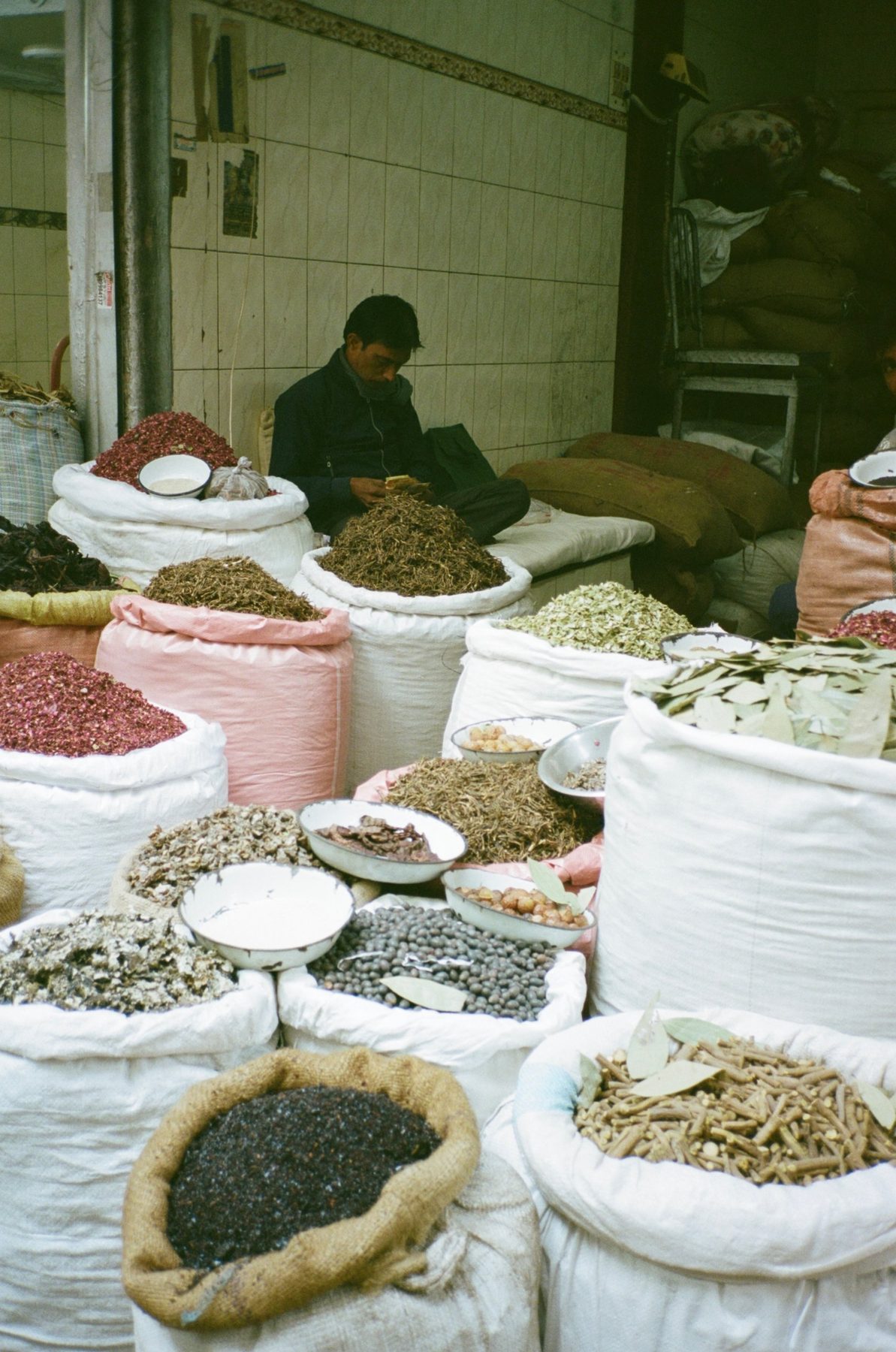 A spice seller counting money behind sacks of rose petals, bark and leaves