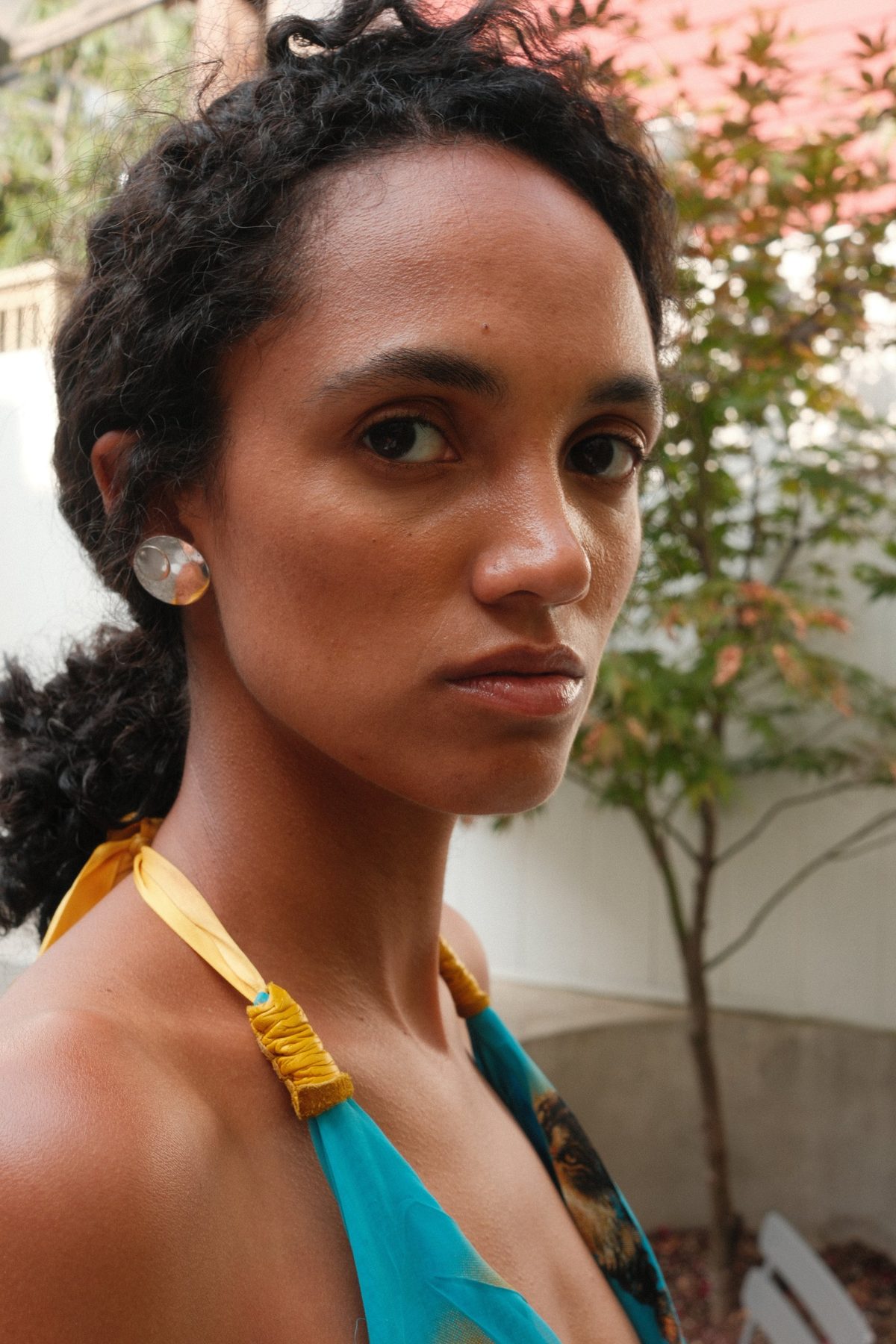 Close portrait of a woman with a steady gaze in a garden courtyard, a silver earring catching light