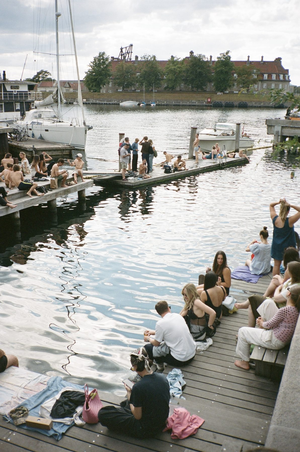 People sitting along a Copenhagen harbor dock above rippling water