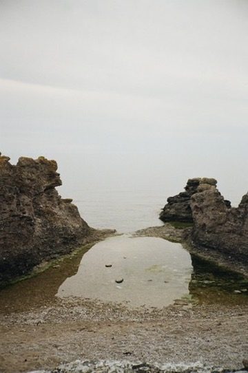 A still tide pool between rocks and the sea