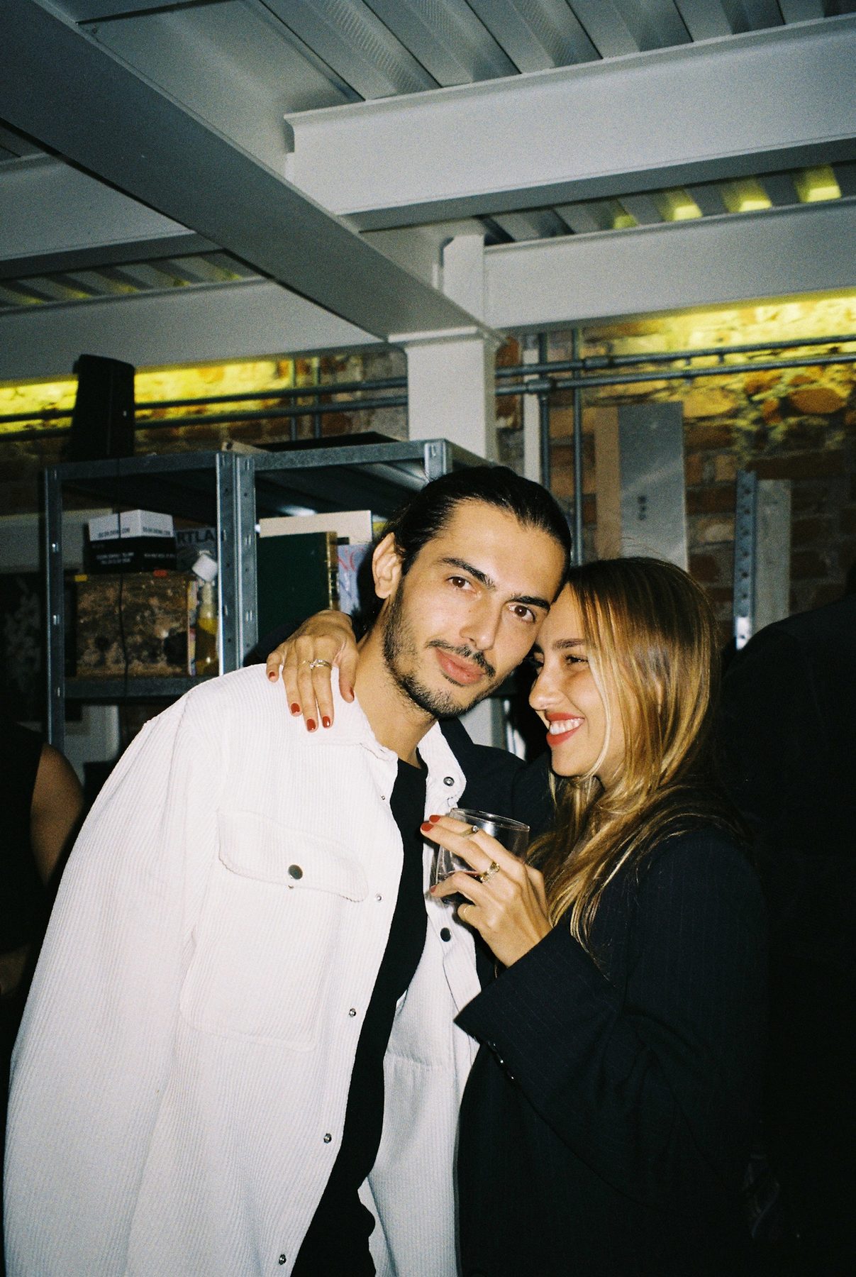 A smiling couple leaning together at a party under white steel beams