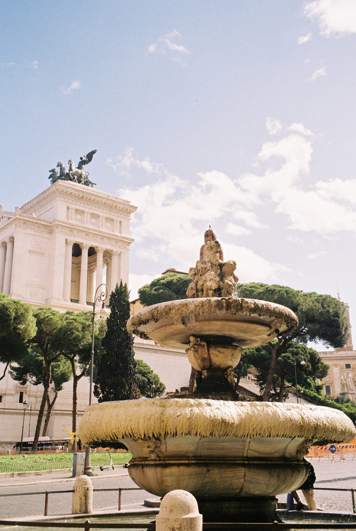 A weathered stone fountain below the white Vittoriano and umbrella pines