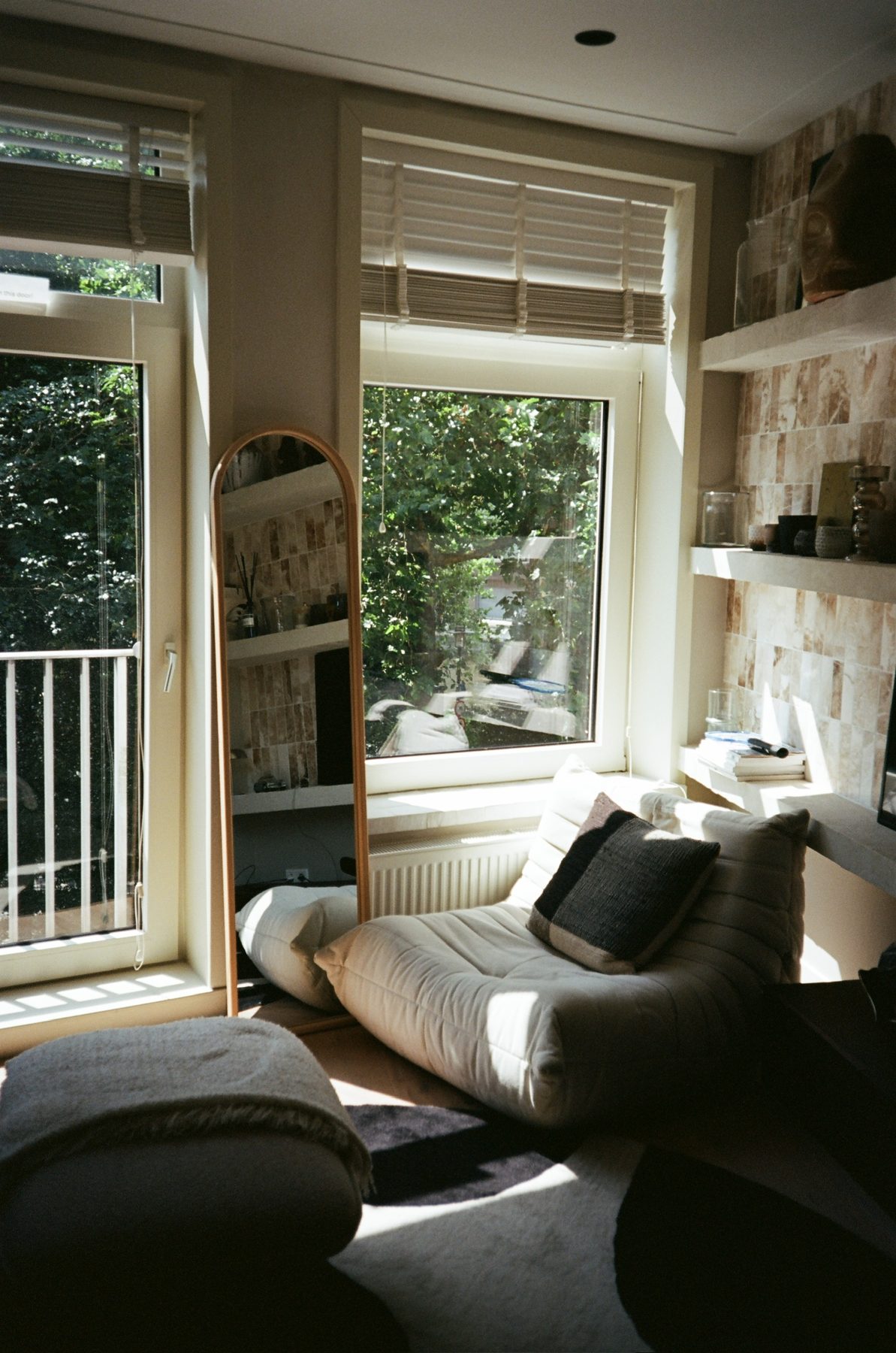 Sunlit apartment corner with a floor mirror, a low sofa and tiled shelves