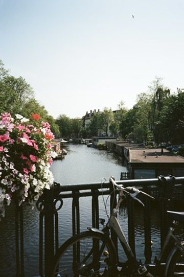 A bike and flower box on a bridge over a houseboat canal