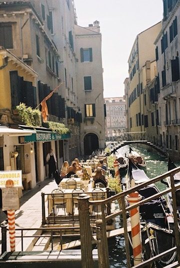 Canal-side restaurant tables beside moored gondolas in Venice