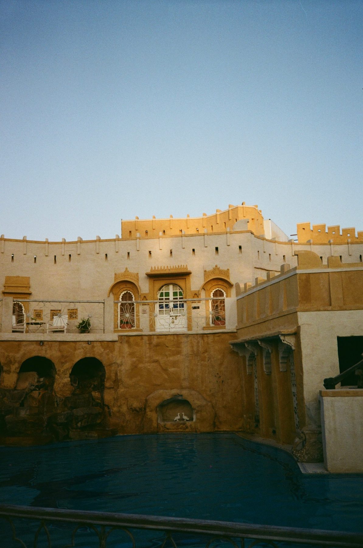 Golden sandstone walls and arched windows above a dark pool at dusk