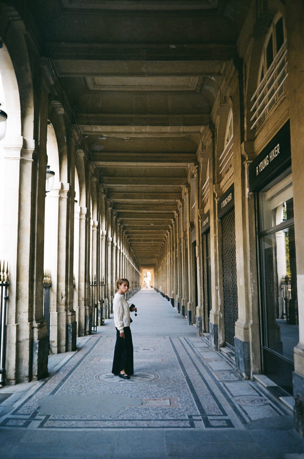 A woman in a cream sweater glancing back in the long Palais-Royal arcade
