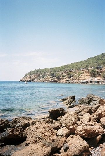 Rocks and clear water below a wooded Ibiza headland