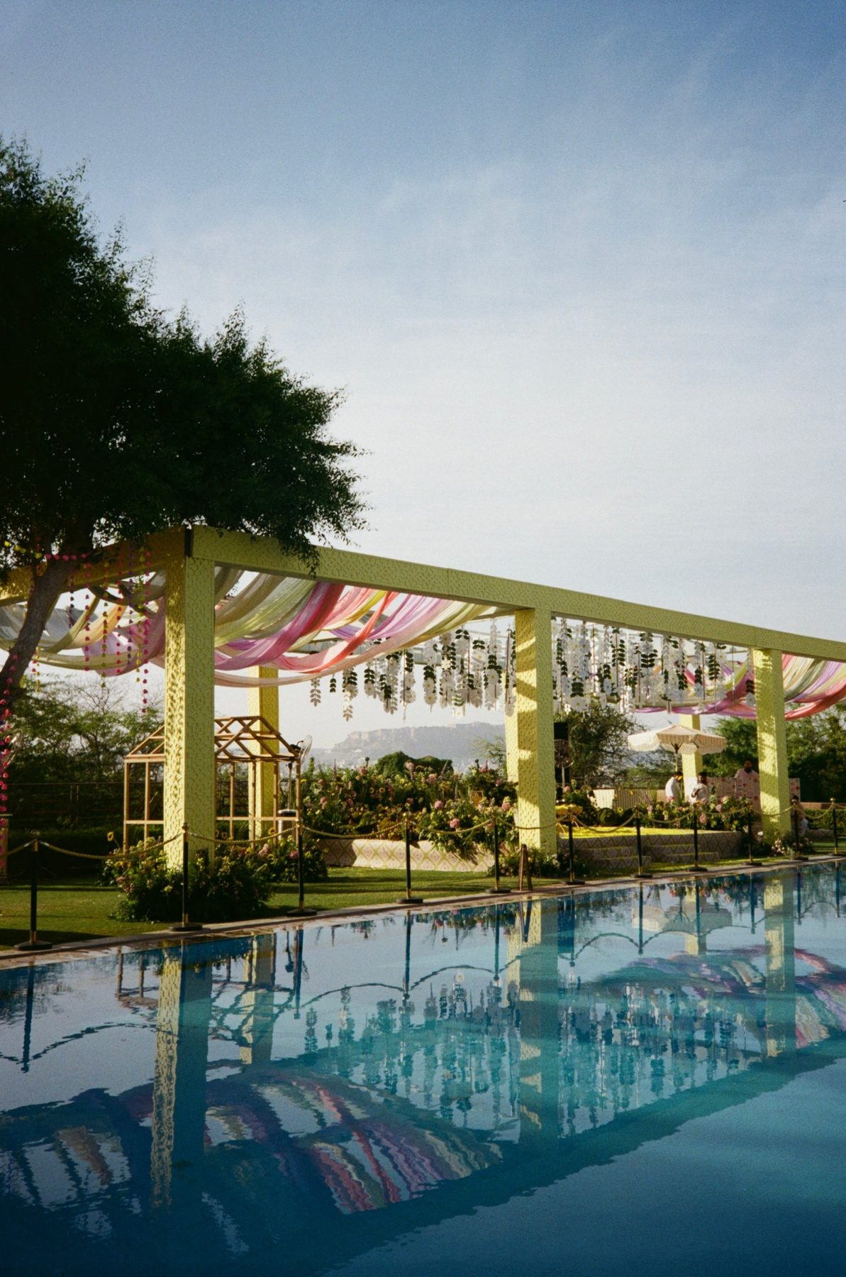 A pergola draped in pastel fabric reflected in a pool, the fort beyond