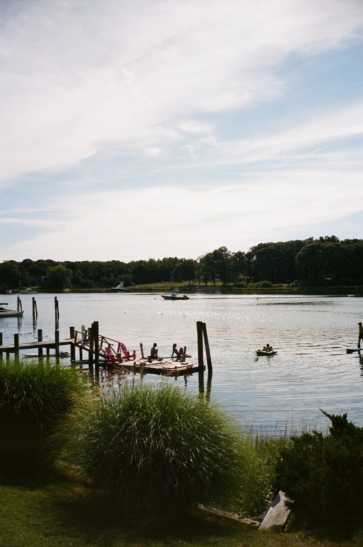 Swimmers on a wooden dock with red chairs on a sunlit lake