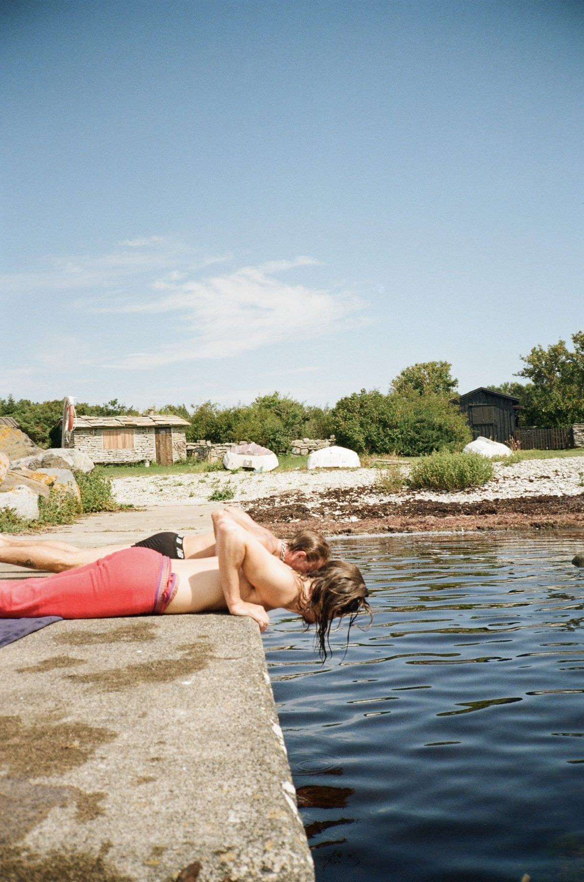 Two people leaning over the edge of a stone pier to kiss above the water