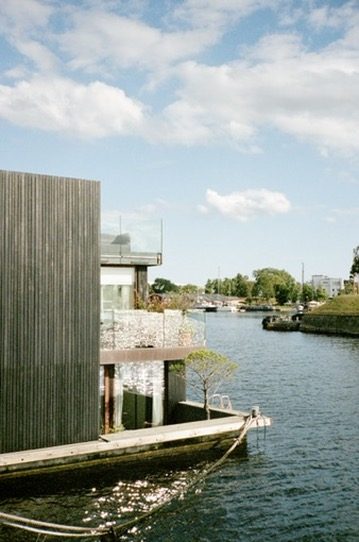 A dark timber house on the water with glinting light
