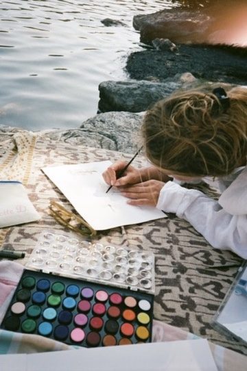 Someone painting in watercolor on a blanket by the water