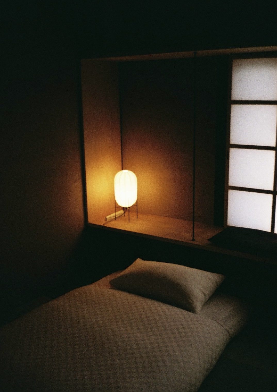 A paper lamp glowing in a dark ryokan alcove beside a futon and shoji screen
