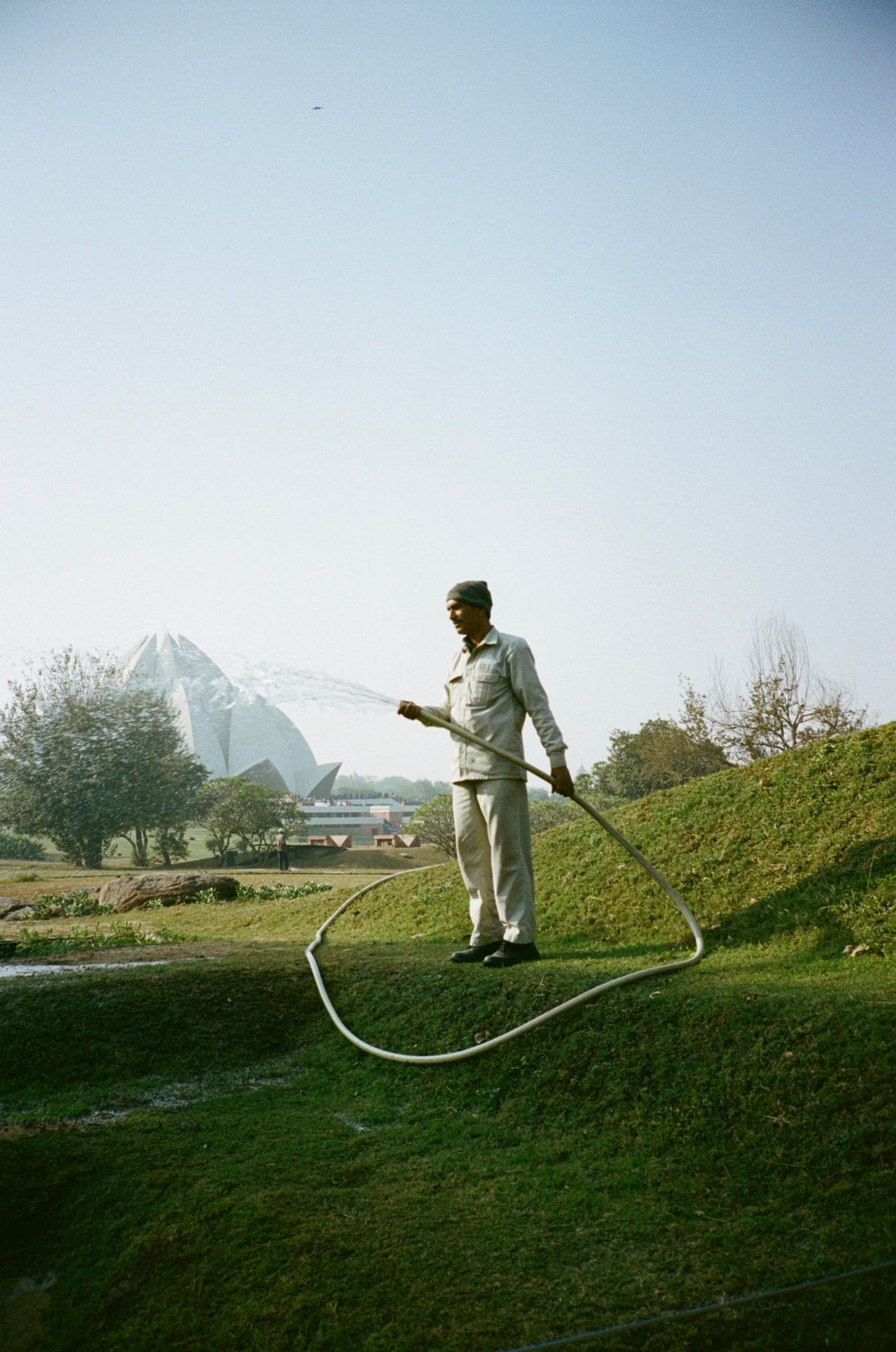 A gardener with a looping hose watering the lawn before the Lotus Temple