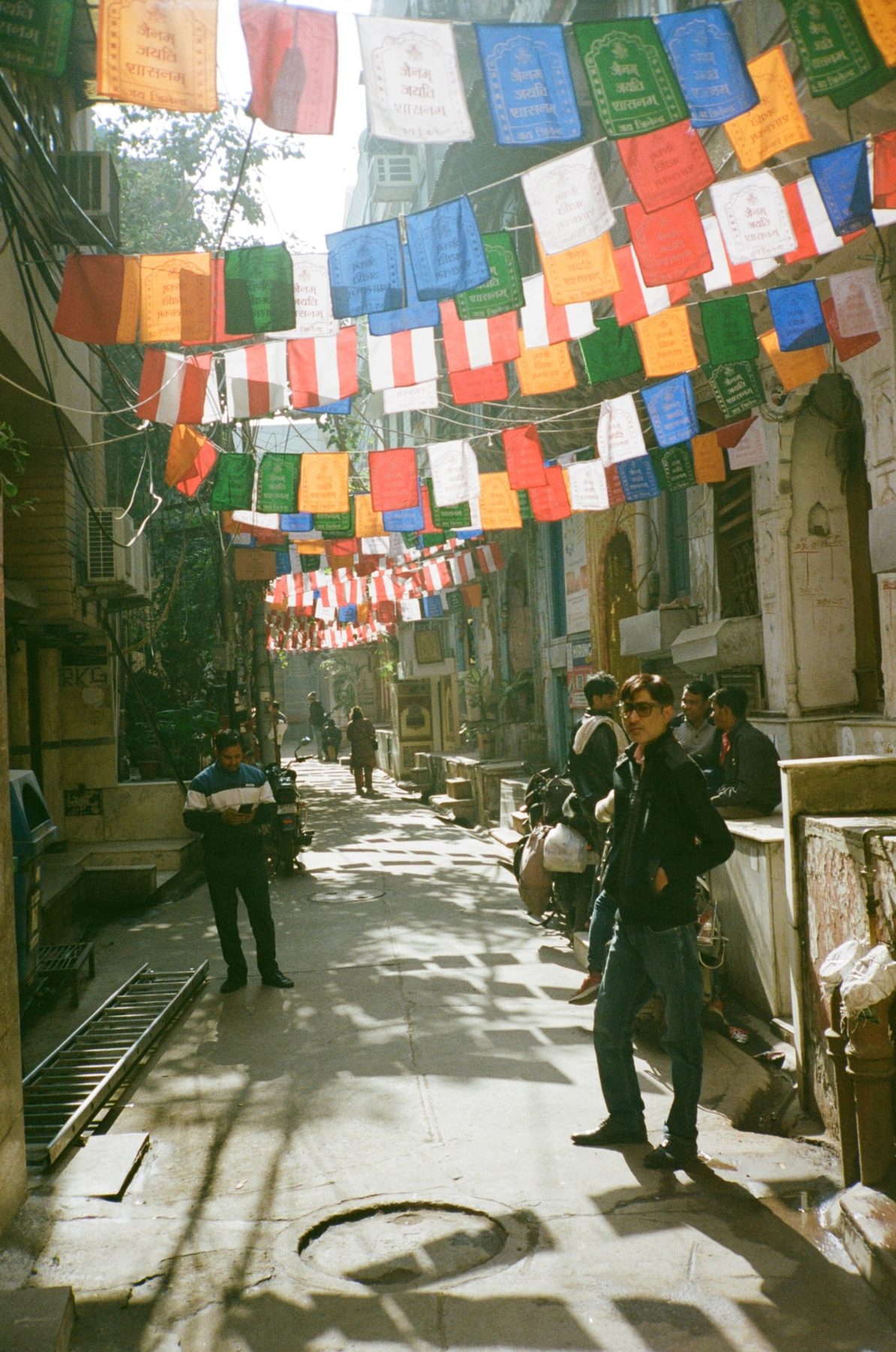 Colorful prayer flags strung over a sunlit Old Delhi lane