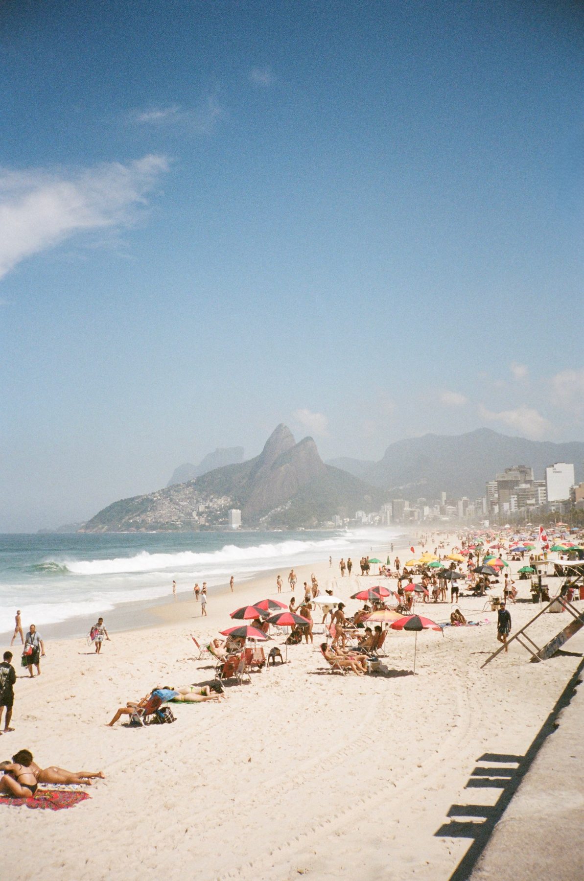Ipanema beach crowded with red umbrellas below Dois Irmãos