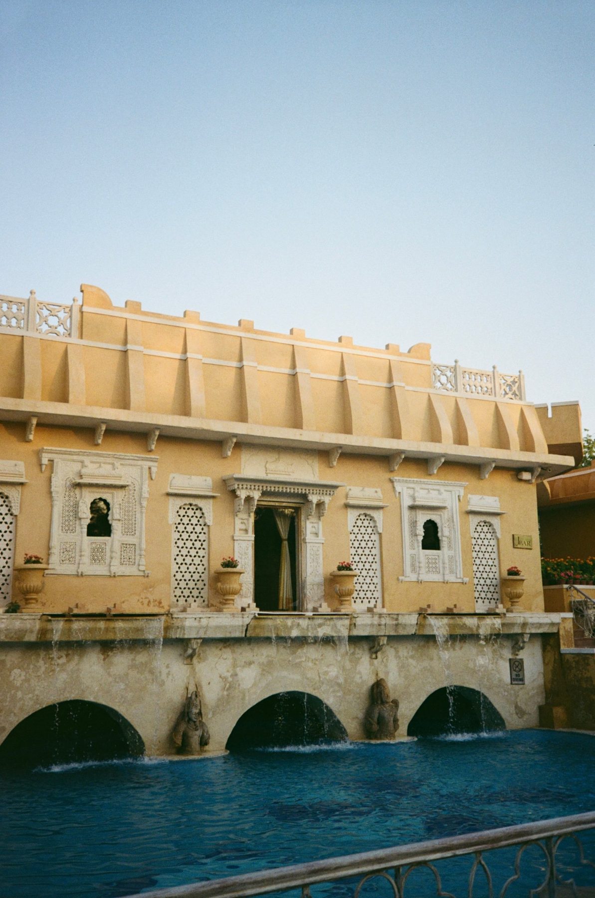 A yellow pavilion with white lattice windows above a fountain pool