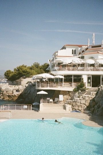 A turquoise pool below a white hotel on the rocks