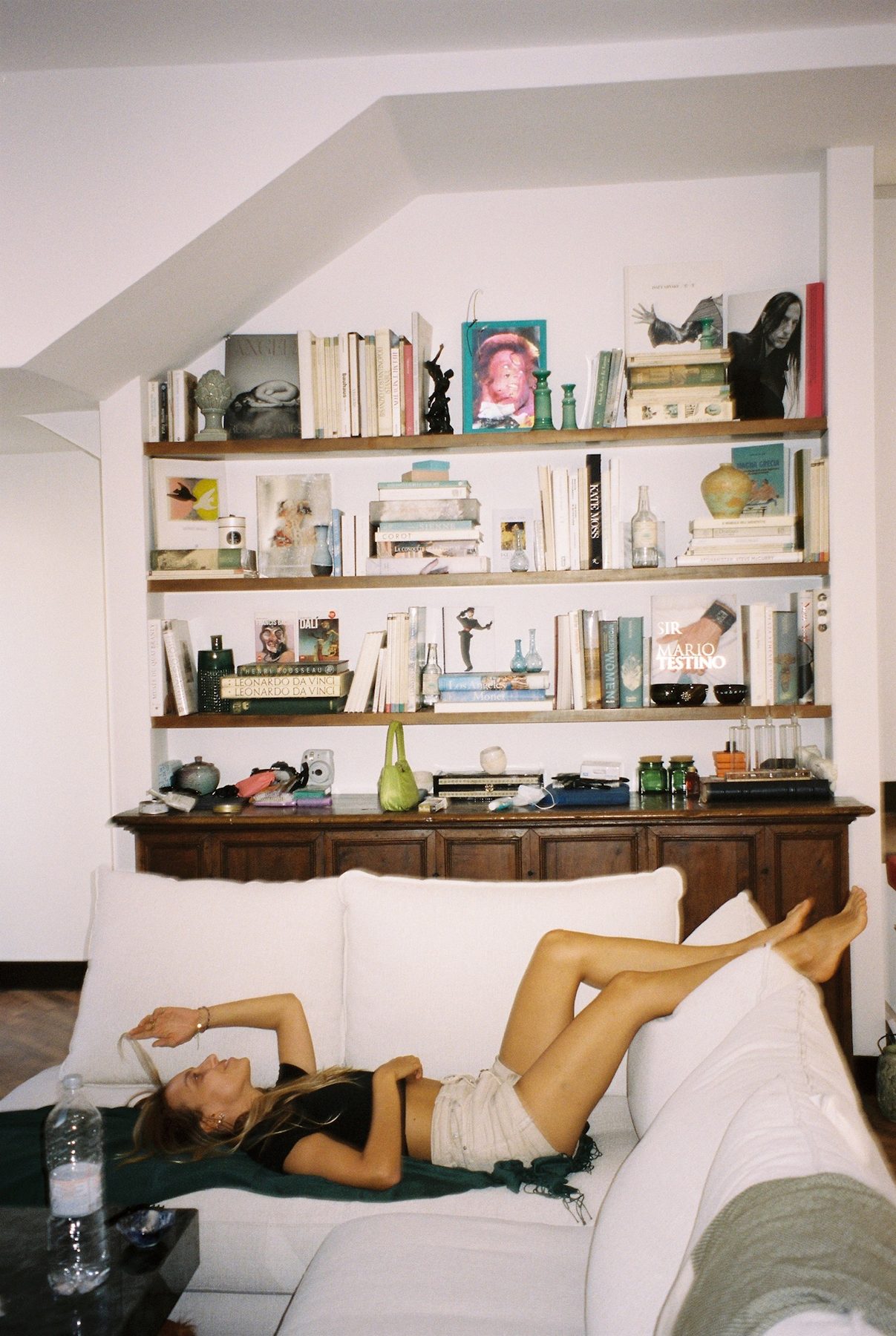 A woman stretched out on a white sofa below shelves of art books