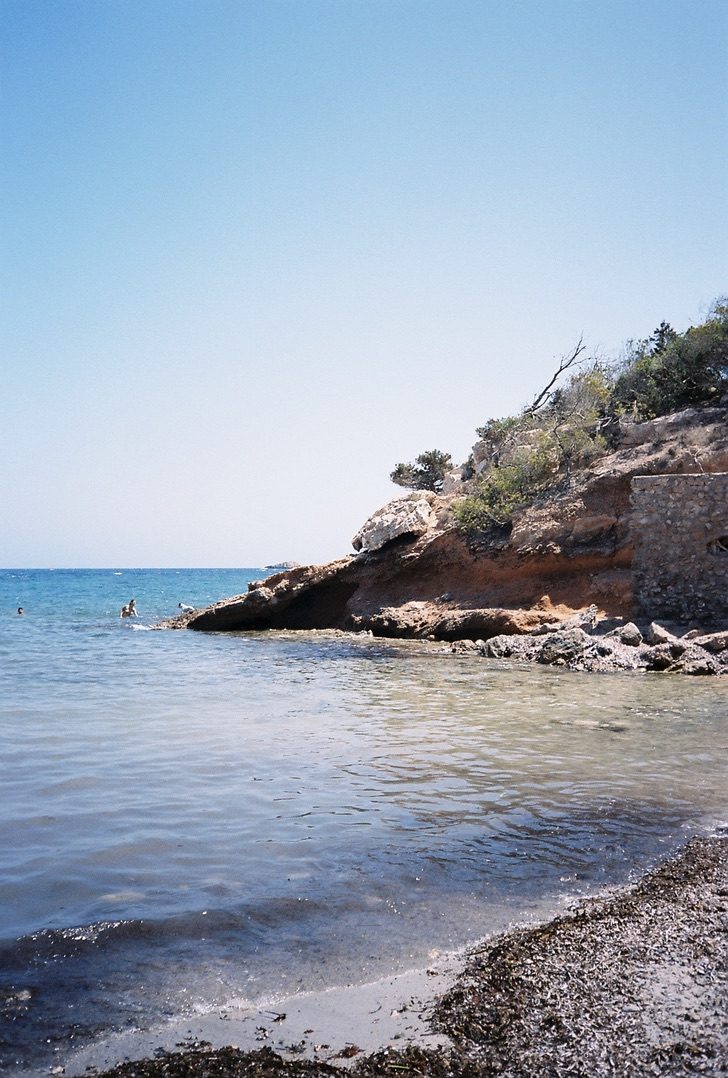 Clear shallow water along a quiet beach below a red rock point
