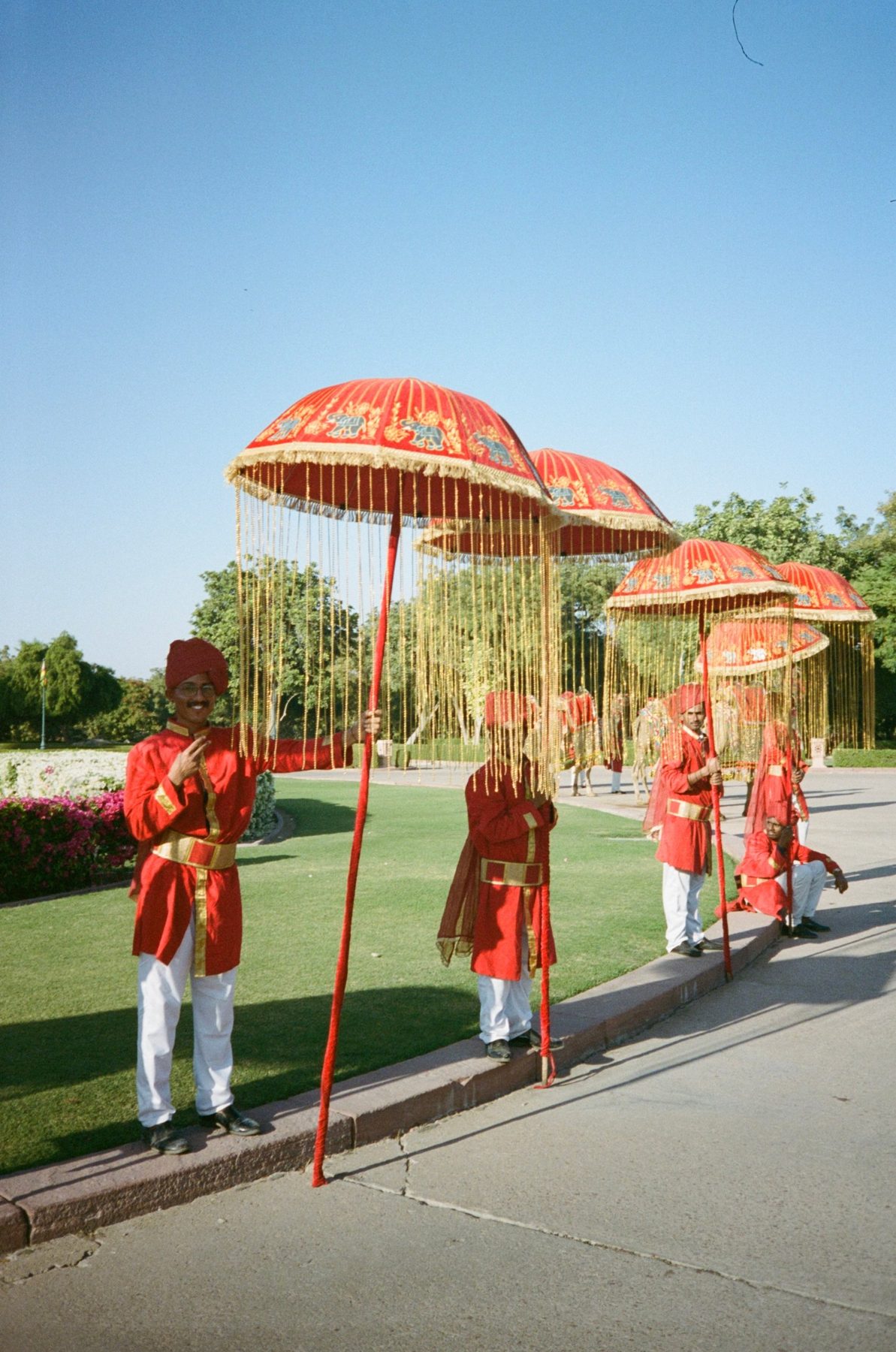 Men in red and gold holding tasselled ceremonial umbrellas along a curb