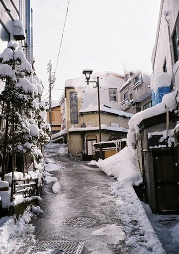 A snowbanked lane in an onsen town under a grey sky