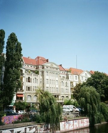 Willows and a pale apartment block above a graffitied Berlin canal