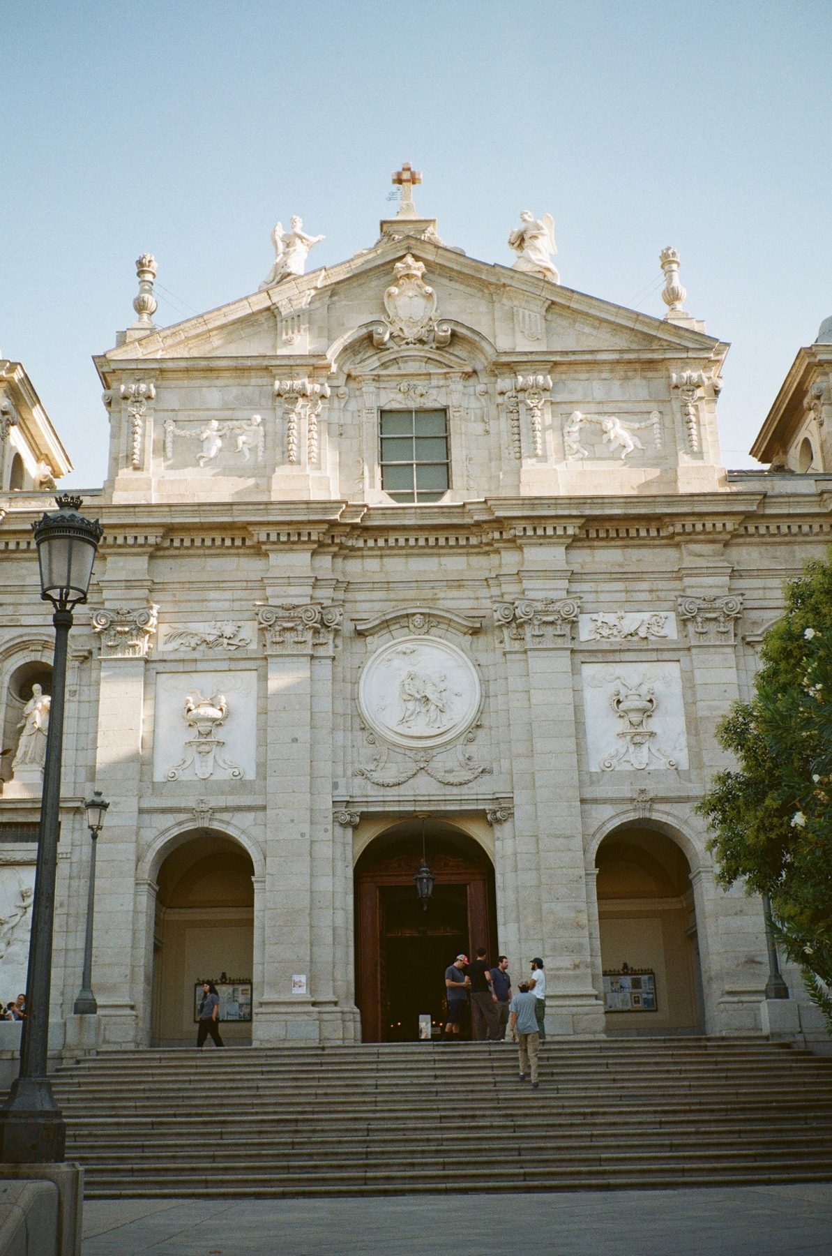 A pale stone church facade with angels on the roof and people on the steps