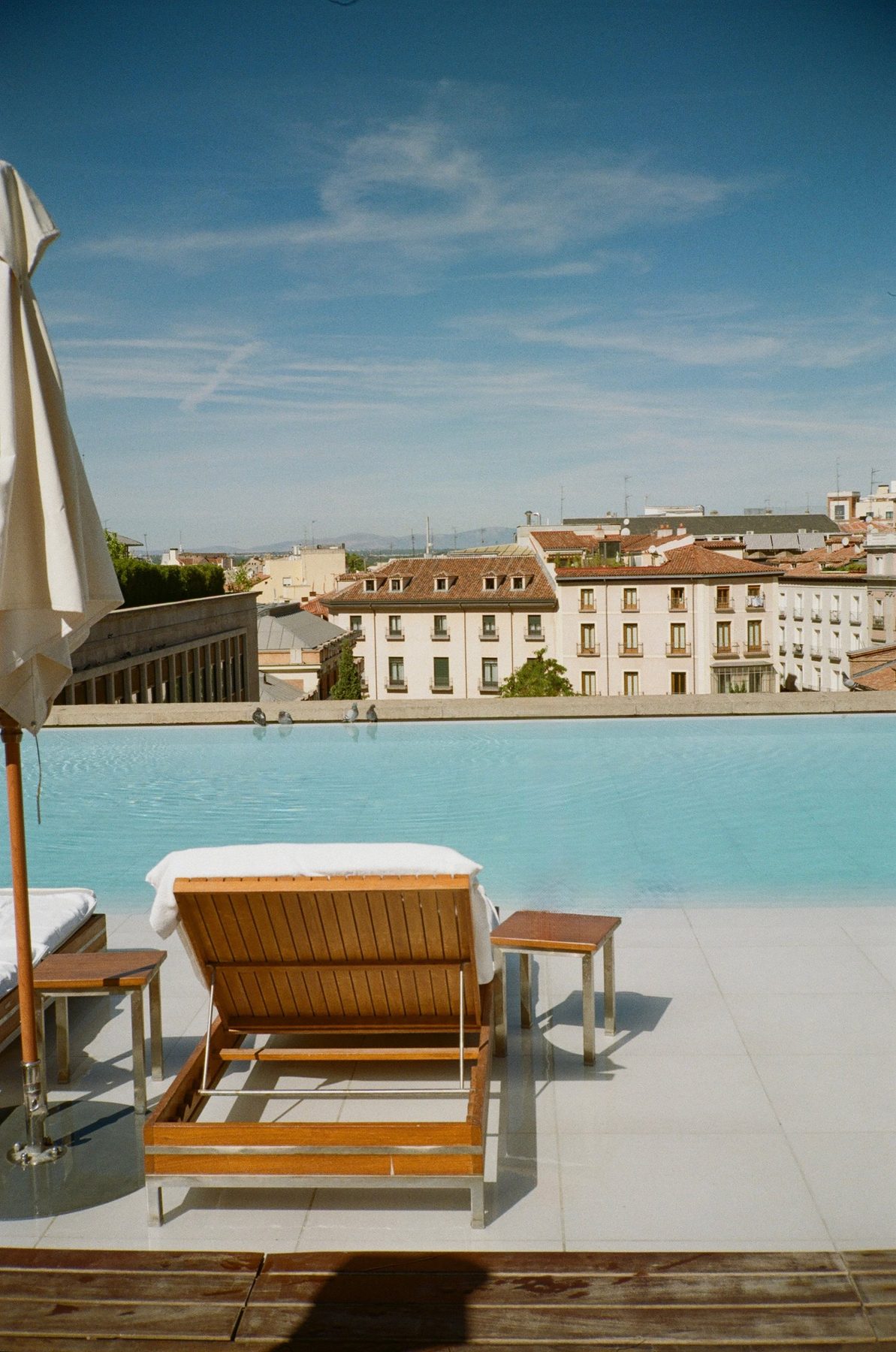 A rooftop pool and lounger above terracotta roofs and a wide blue sky