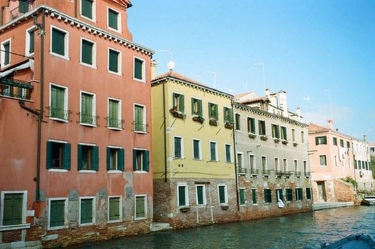 Red, yellow and grey palazzi with green shutters along a sunny Venetian canal