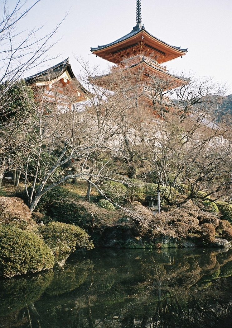 The vermilion pagoda of Kiyomizu-dera above bare winter trees, reflected in a still pond
