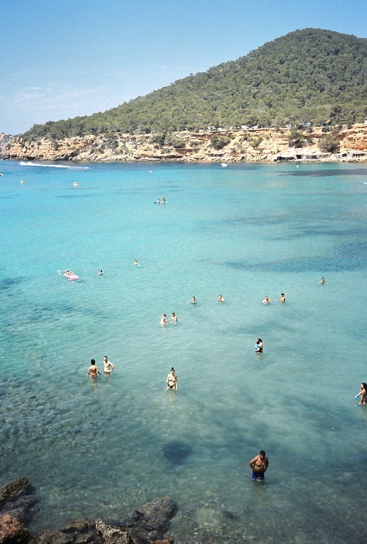 Swimmers scattered across a turquoise bay below a wooded hill